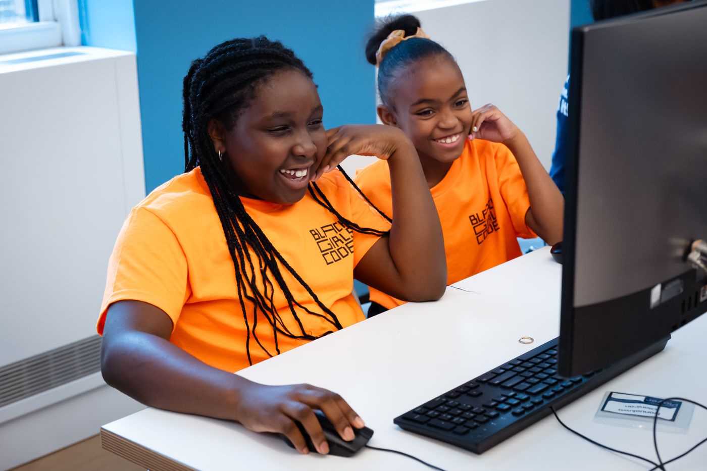 Two students laughing while coding at a computer